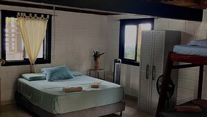A bedroom with a bed, a window with curtains, a radiator, and a wardrobe. - Las Rocas Village Ecohotel  (Acandi)