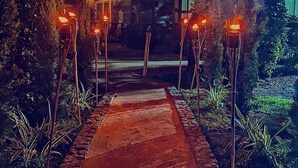 A pathway leading to a building with a traditional architectural style, surrounded by lush vegetation and illuminated by multiple light fixtures. - Las Rocas Village Ecohotel  (Acandi)