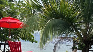 A beachside seating area with a red umbrella, a red chair, and a table with coconuts and a drink. - Las Rocas Village Ecohotel  (Acandi)