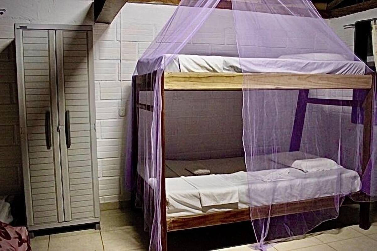 Ein Einzelzimmer mit einem hölzernen Etagenbett, einem Kleiderschrank und einem Moskitonetz.