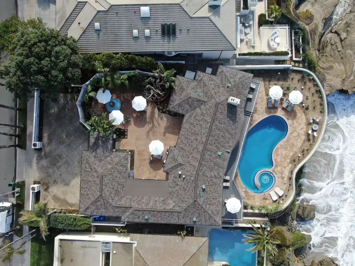An aerial view of a resort with a large pool, outdoor seating, and a rocky shoreline.