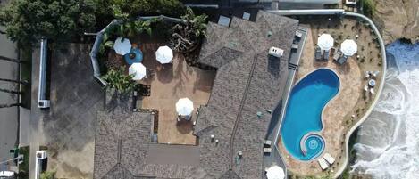 An aerial view of a resort with a large pool, outdoor seating, and a rocky shoreline.