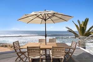 A wooden deck with a table and chairs, an umbrella, and a view of the ocean. - Beachfront Windansea Escape ideal for families (San Diego)