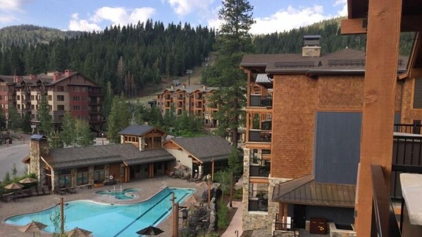 A resort with a swimming pool, multiple buildings, and a mountainous backdrop. - Surrounded by pine trees and mountains (Truckee)