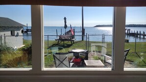 A view through a window of a lakeside property with a picnic table, chairs, and an American flag.