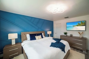 A bedroom with a bed, nightstands, a dresser, a television, and a wall-mounted picture. - Modern 6BR Home - Jacuzzi, BBQ, Game Room (Miami)