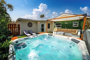 A backyard with a hot tub, a covered seating area, and a dartboard. - Modern 6BR Home - Jacuzzi, BBQ, Game Room (Miami)