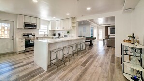 A modern kitchen with white cabinets, a central island with stools, and a dining area with a pool table. - Modern 6BR Home • Jacuzzi_BBQ, Game Room & Games (Miami)