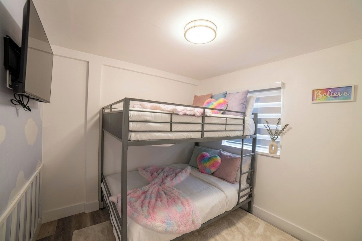 A bunk bed room with a television mounted on the wall, a window with blinds, and a motivational sign on the wall.