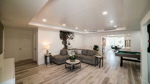 A spacious living room with a pool table, a sectional sofa, and a wall mural. - Modern 6BR Home • Jacuzzi_BBQ, Game Room & Games (Miami)