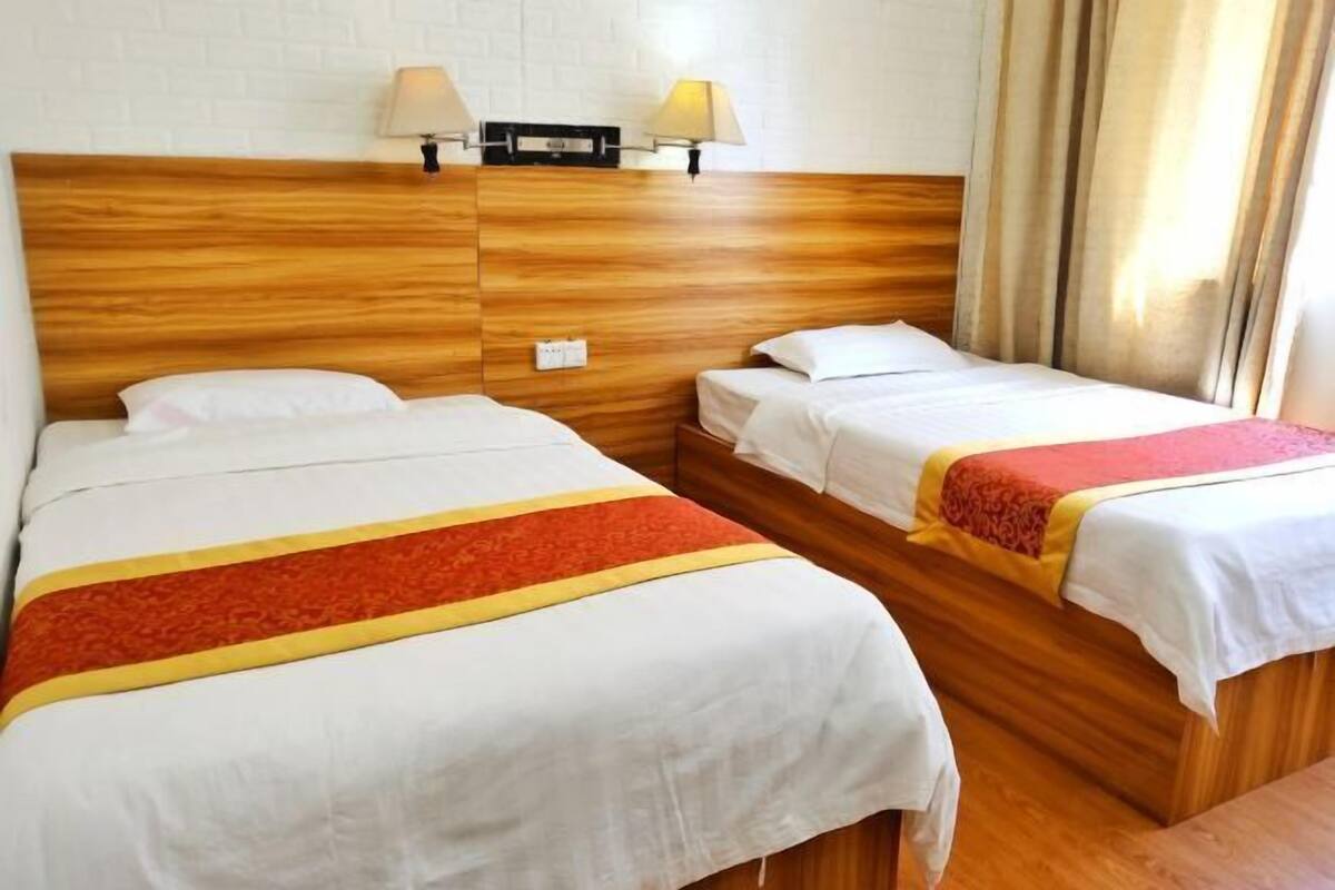 Quarto de hotel com duas camas, cabeceiras de madeira, roupa de cama branca e duas luminárias fixadas na parede.