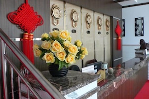 Una recepción con un jarrón de flores amarillas, un adorno rojo y un reloj de pared.