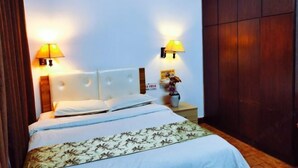 Ein Hotelzimmer mit einem Bett, zwei Wandlampen, einem Nachttisch und einem dunklen Holzschrank.
