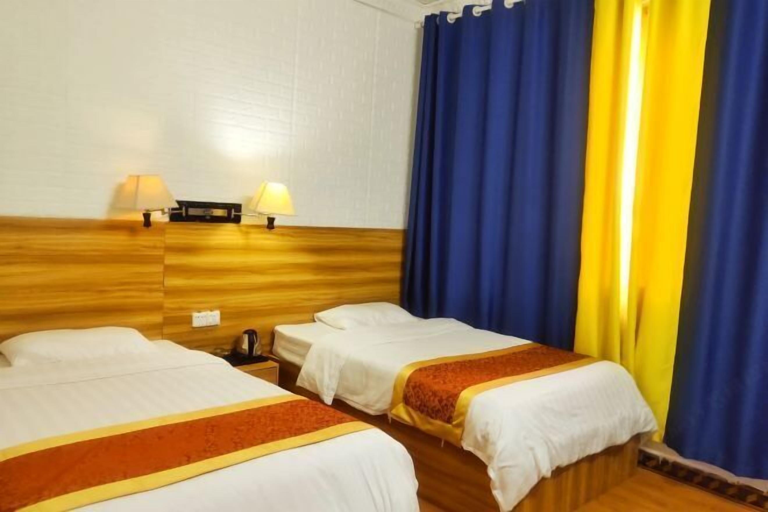 Ett hotellrum med två separata sängar, en sänggavel i trä, två sänglampor och ett litet bord vid sängen med en vattenkokare.
