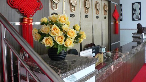 Ein Hotel-Rezeptionsbereich mit einer Marmor-Theke, einer Vase mit gelben Rosen und traditioneller chinesischer Dekoration.
