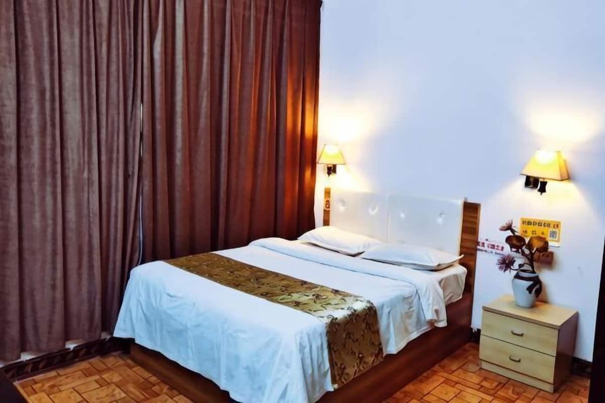 Quarto de hotel com cama, mesas de cabeceira e cortinas.