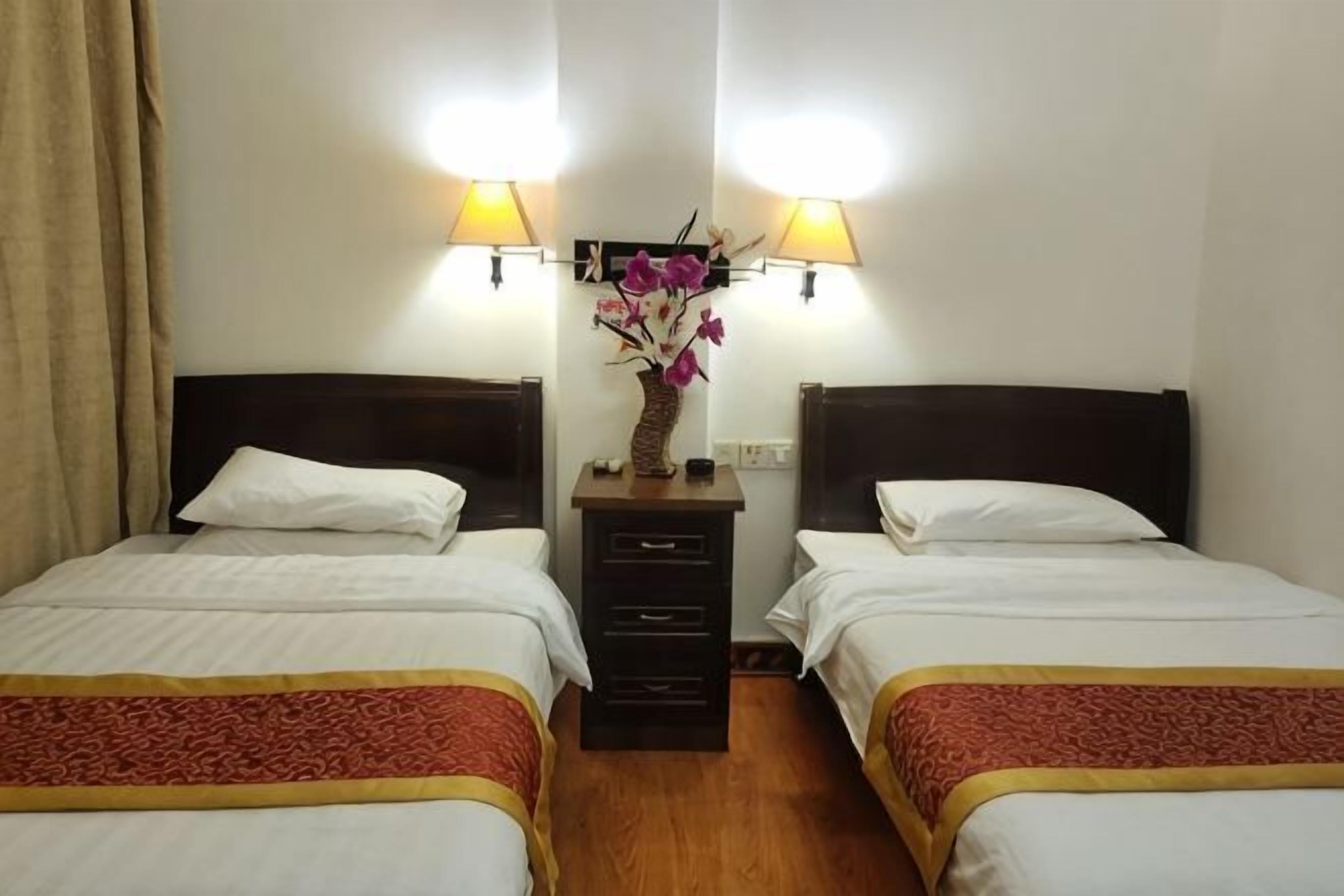 A hotel room with two beds, a nightstand, and two wall-mounted lamps.