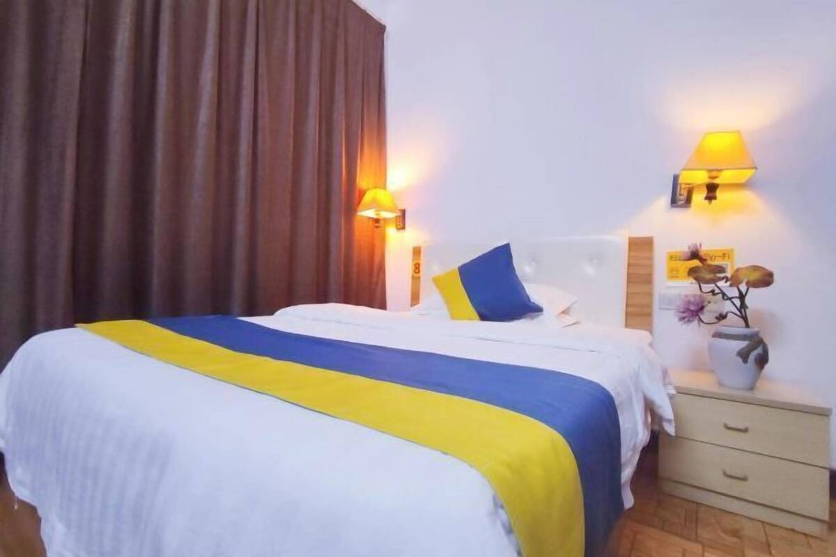 Quarto de hotel com cama, duas luminárias de cabeceira, mesa de cabeceira com um vaso e cortina.