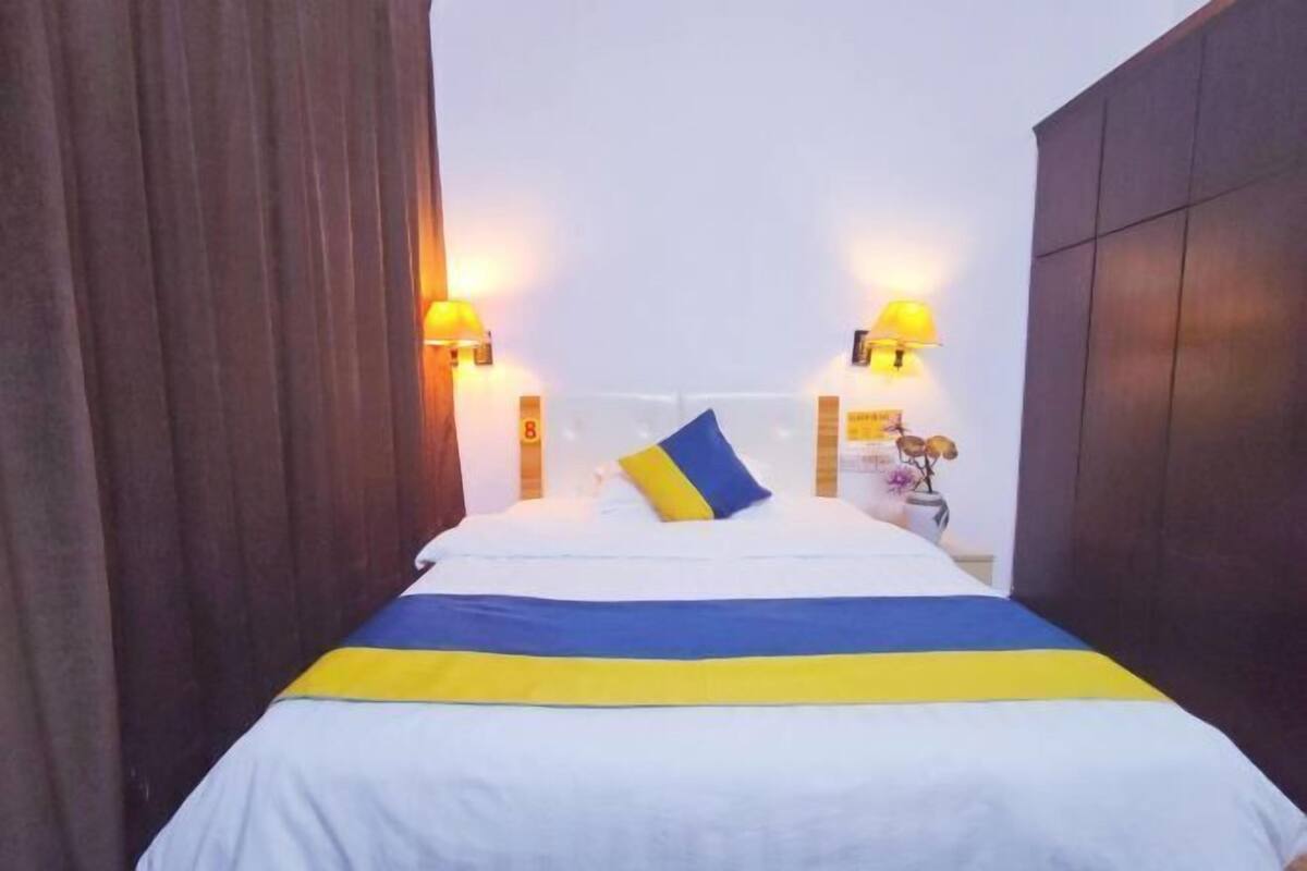 Uma cama com colcha listrada em branco e azul, duas luminárias na parede e uma mesa de cabeceira com um vaso de flores.