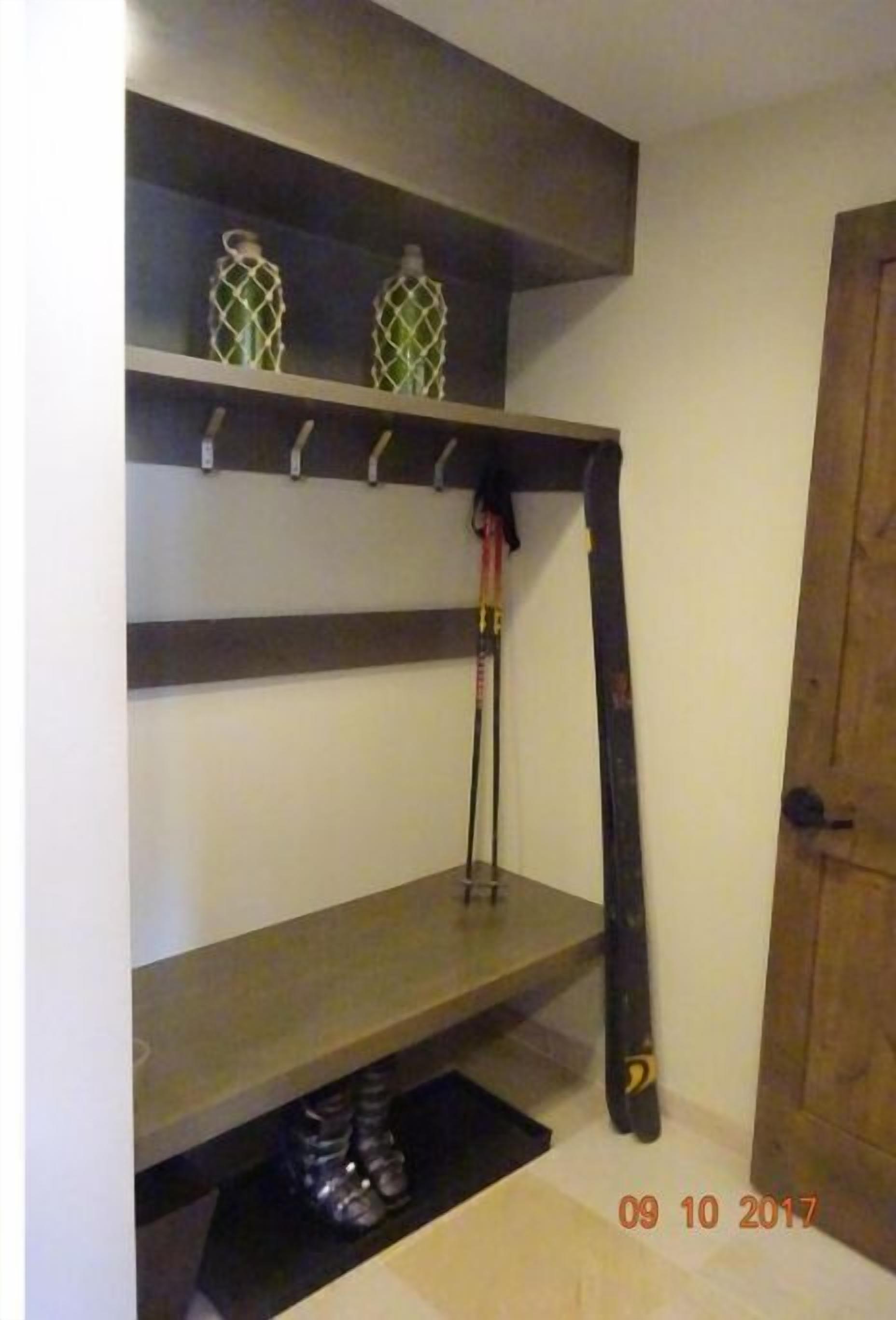 A room with a wooden door, a shelf with two decorative bottles, and a pair of skis leaning against the wall.