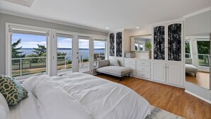 A bedroom with a large bed, a sofa, a desk, and a view of the ocean. - Luxury Water View 6BR Retreat with Gym (Seattle)