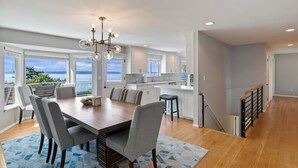 A modern kitchen with white cabinets, a wooden dining table, and a view of the sea. - Luxury Water View 6BR Retreat with Gym (Seattle)