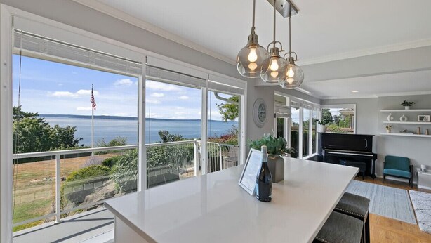 A modern kitchen with large windows, a piano, and a view of the sea. - Luxury Water View 6BR Retreat with Gym (Seattle)