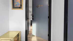 A hallway with a framed abstract painting, a welcome sign, and a wooden bench. - Cozy Studio in the Crossroads | 69 (Kansas City)