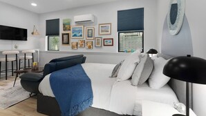A modern bedroom with a large bed, a desk with two chairs, and a TV mounted on the wall. - Cozy Studio in the Crossroads | 69 (Kansas City)
