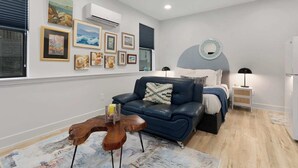 A modern living room with a blue sofa, a wooden coffee table, and a bed with a round mirror. - Cozy Studio in the Crossroads | 69 (Kansas City)