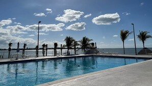 A clear blue sky with clouds, a swimming pool with lounge chairs, and palm trees. - Ocean Isles Breeze Getaway – Marathon Oi#82 (Marathon)