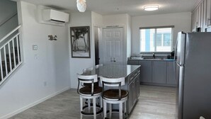 A modern kitchen with a central island, bar stools, a refrigerator, and a window with blinds. - Ocean Isles Breeze Getaway – Marathon Oi#82 (Marathon)