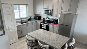 A modern kitchen with granite countertops, stainless steel appliances, and a central island with four chairs. - Ocean Isles Breeze Getaway – Marathon Oi#82 (Marathon)