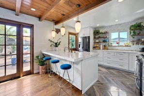 A kitchen with a large island, bar stools, wooden flooring, and a view through glass doors.