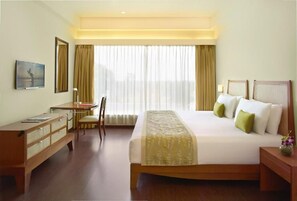 A hotel room with a bed, desk, chair, and a large window with curtains. - Ginger Gondia, Balaghat Road (Gondia)