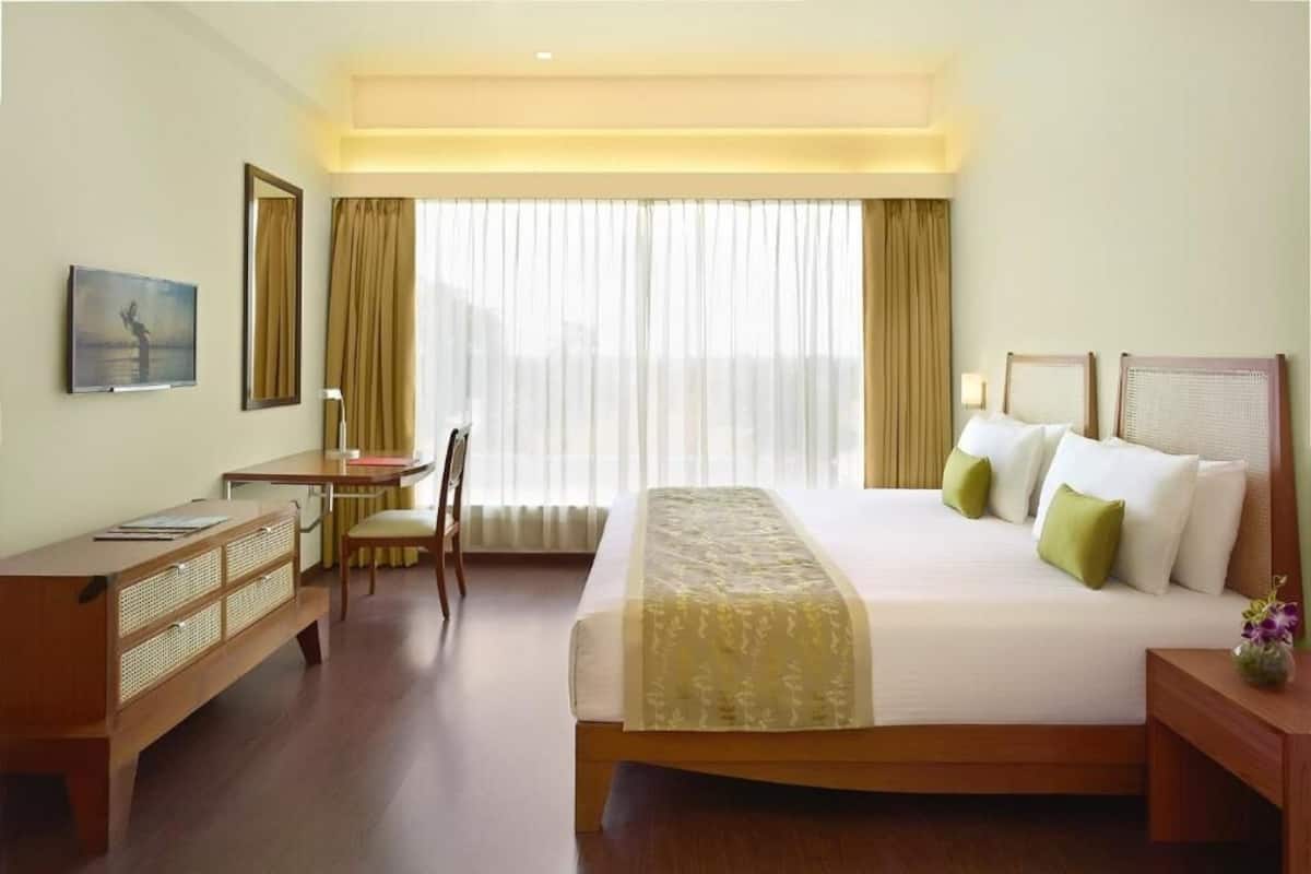 Une chambre d’hôtel avec un lit, un bureau, une chaise et une grande fenêtre avec des rideaux.
