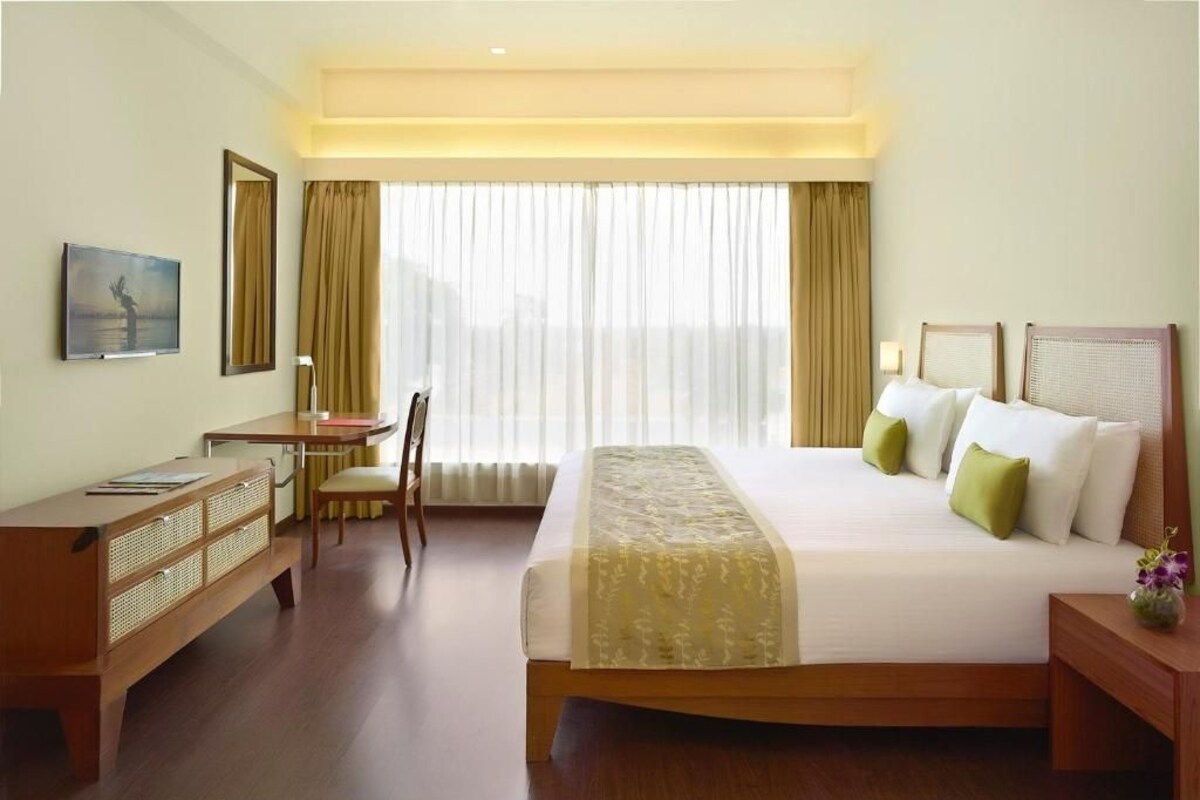 A hotel room with a bed, desk, chair, and a large window with curtains.