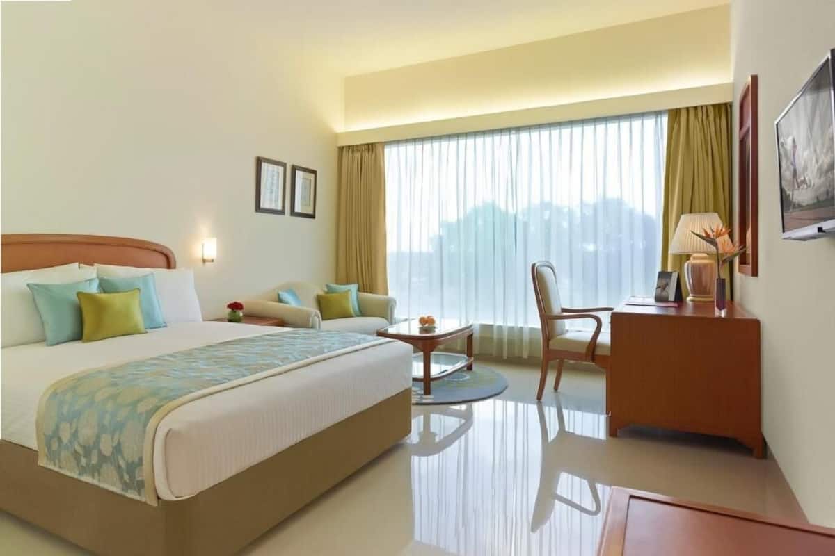 Une chambre d’hôtel avec un grand lit, un bureau, une chaise et une fenêtre avec des rideaux.