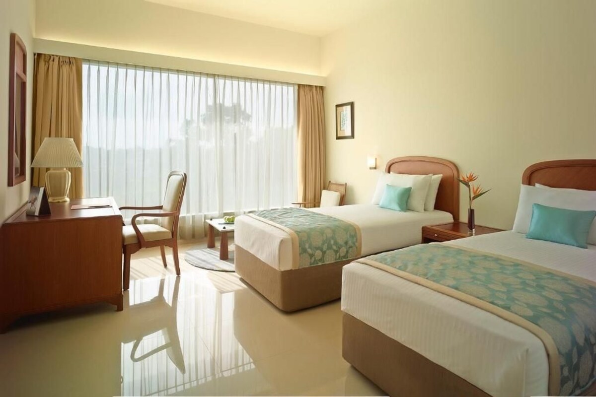 A hotel room with two beds, a desk, a chair, and a large window with curtains.