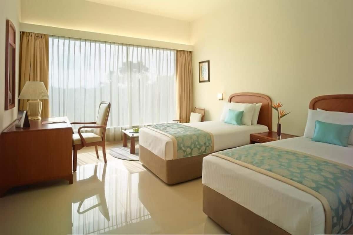 Une chambre d’hôtel avec deux lits, un bureau, une chaise et une grande fenêtre avec des rideaux.