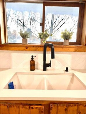 A kitchen with a large window, a black faucet, and two potted plants on the windowsill.