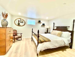 A bedroom with a wooden four-poster bed, a dresser, a chair, a TV, and a mirror.