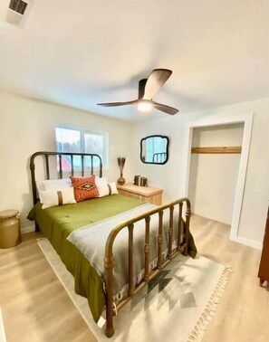 Een slaapkamer met een bed, een plafondventilator, een raam, een nachtkastje en een kledingkast.