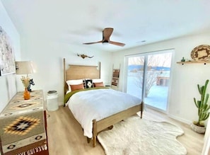 A bedroom with a bed, a ceiling fan, a window, and a cactus plant.