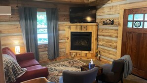 A cozy log cabin interior with a fireplace, comfortable seating, and a television. - Cozy, Quiet Cabin Under the Stars - Near Desoto State Park and Downtown Mentone! (Mentone)