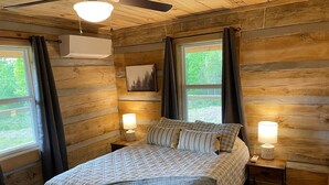 A cozy log cabin bedroom with a bed, two bedside lamps, a ceiling fan, and a window with curtains. - Cozy, Quiet Cabin Under the Stars - Near Desoto State Park and Downtown Mentone! (Mentone)