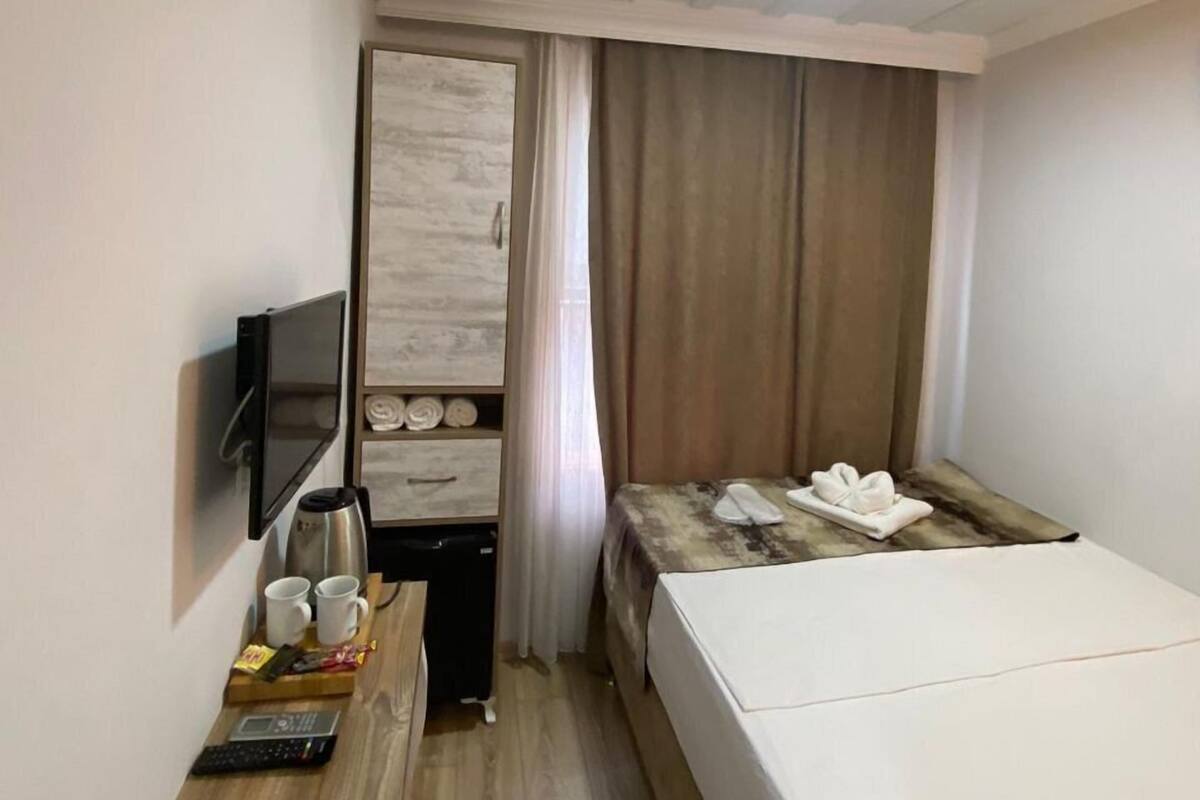 A hotel room with a bed, a desk with a laptop, a TV mounted on the wall, and a small table with a coffee maker and cups.