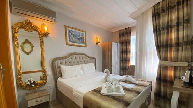 A hotel room with a large bed, a wooden nightstand, a mirror with an ornate frame, a wall-mounted light, and a painting. - New Cherry Hotel (Istanbul)