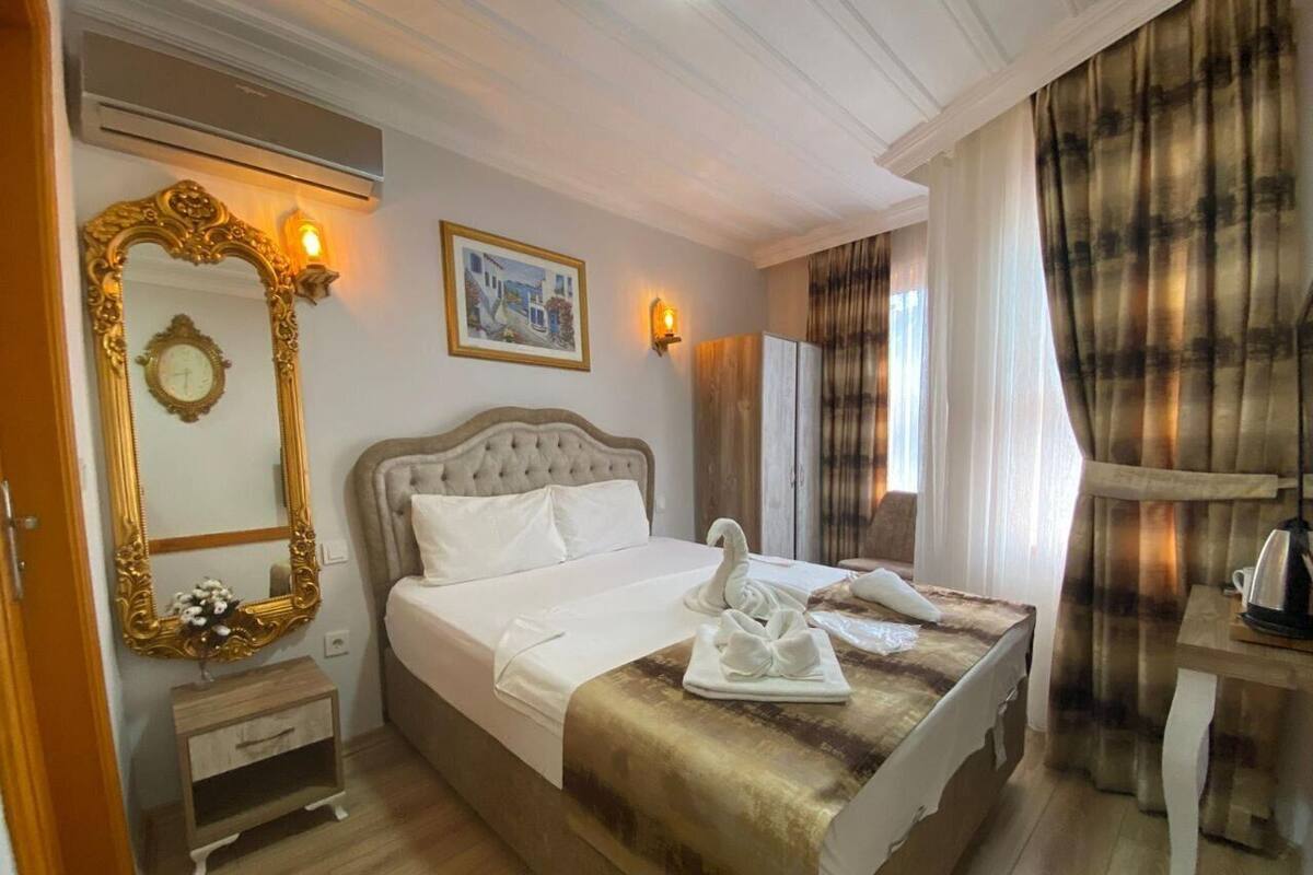 A hotel room with a large bed, a wooden nightstand, a mirror with an ornate frame, a wall-mounted light, and a painting.