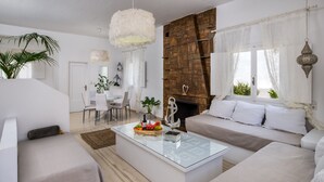 A modern living room with a glass coffee table, beige sofas, and a stone accent wall. - Sol Mare Salis (Santorini)